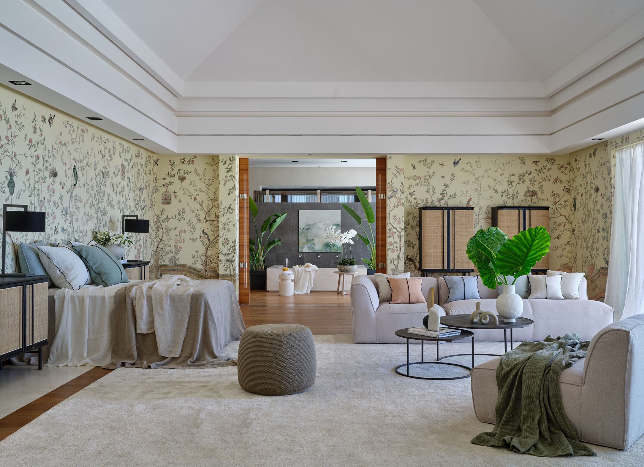 Suite principal de gran formato con papel pintado botánico de aves y flores en toda la habitación, cama con ropa en lino gris azulado, zona de estar con sofás y acceso a vestidor.