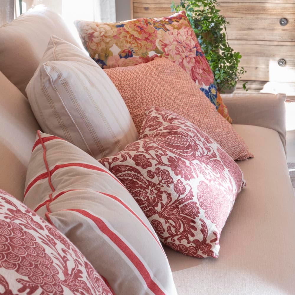 Primer plano de los cojines del sofá del salón que combinan estampados toile granate, rayas rojas, tejido de punto terracota y floral multicolor vintage, reflejando la riqueza textil y la mezcla de estampados característica del proyecto.