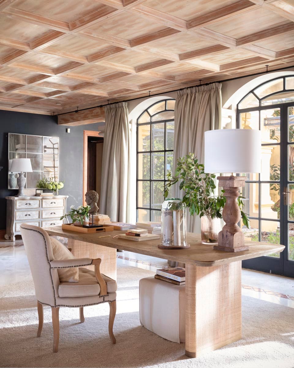 El despacho desde otro ángulo muestra la pared de fondo en color antracita que contrasta con el techo artesonado de madera clara y el escritorio de roble blanqueado. La cómoda vintage decapada, el espejo de cuarterones y los ventanales de acero crean un ambiente de estudio clásico y sofisticado.