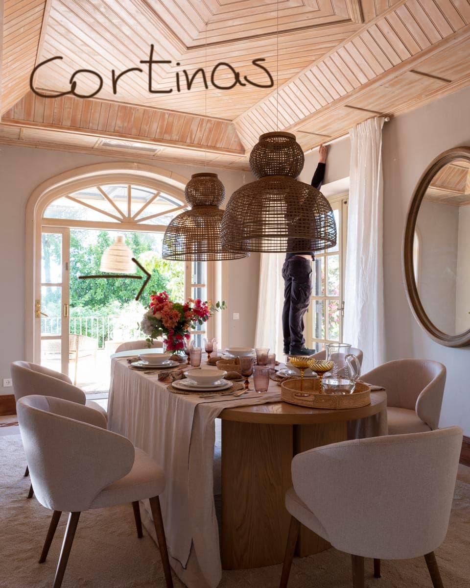 Fotografía de referencia de obra del comedor durante la instalación de cortinas, con anotación manuscrita 'Cortinas' y flecha indicativa. Muestra la mesa oval, las lámparas de ratán y el techo octogonal de madera en proceso de montaje.